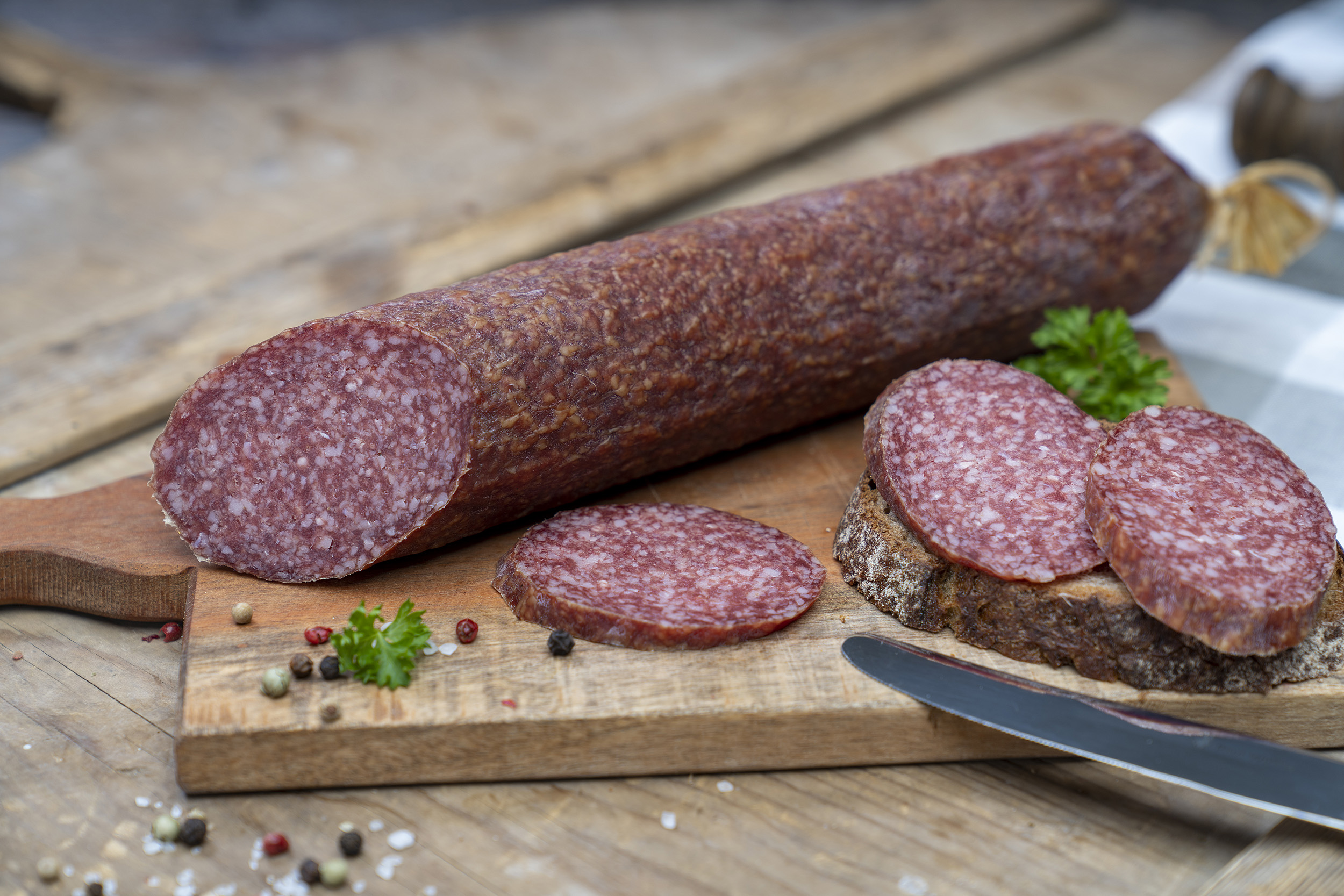 Eine Bauernsalami auf einem Brett. Daneben ein paar Scheiben der Wurst und Brot. 