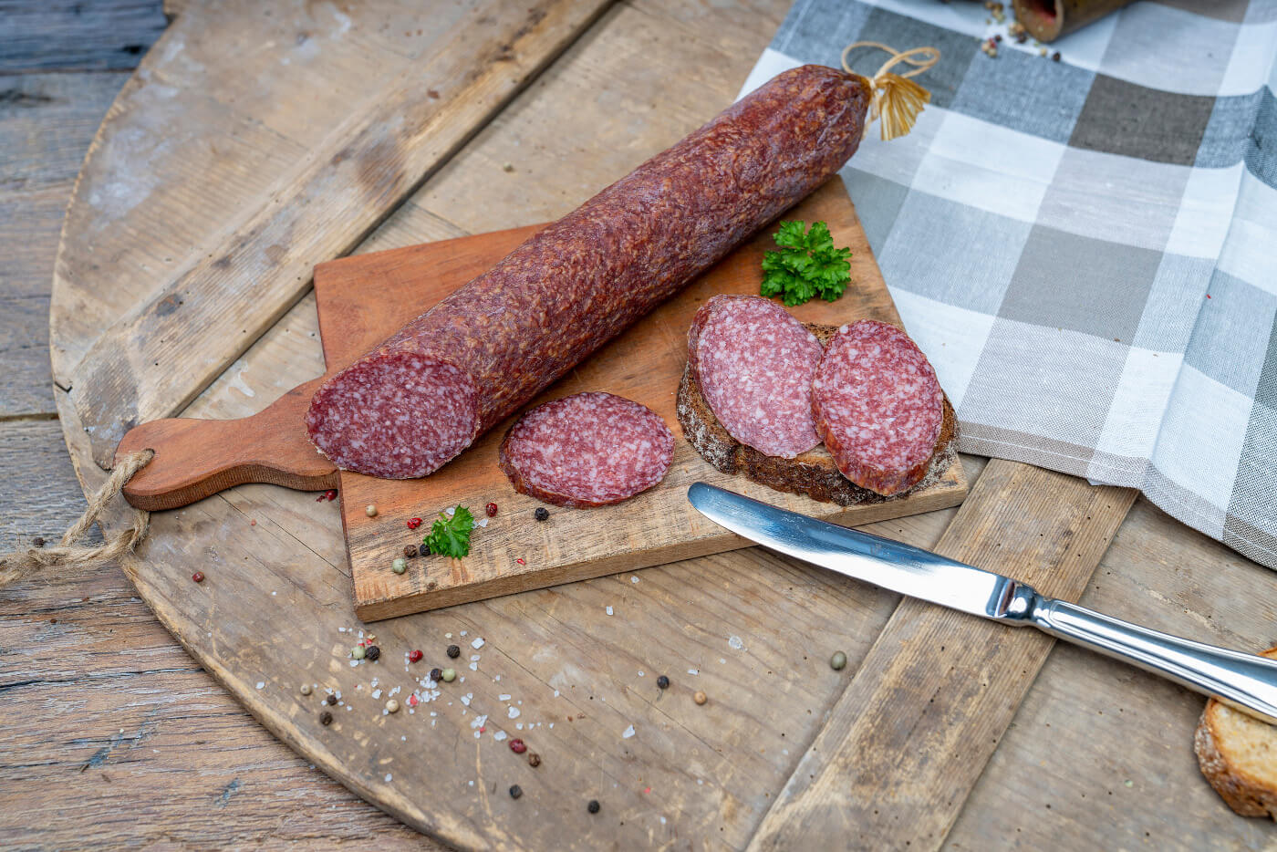 Eine Bauernsalami auf einem Brett. Daneben ein paar Scheiben der Wurst und Brot.