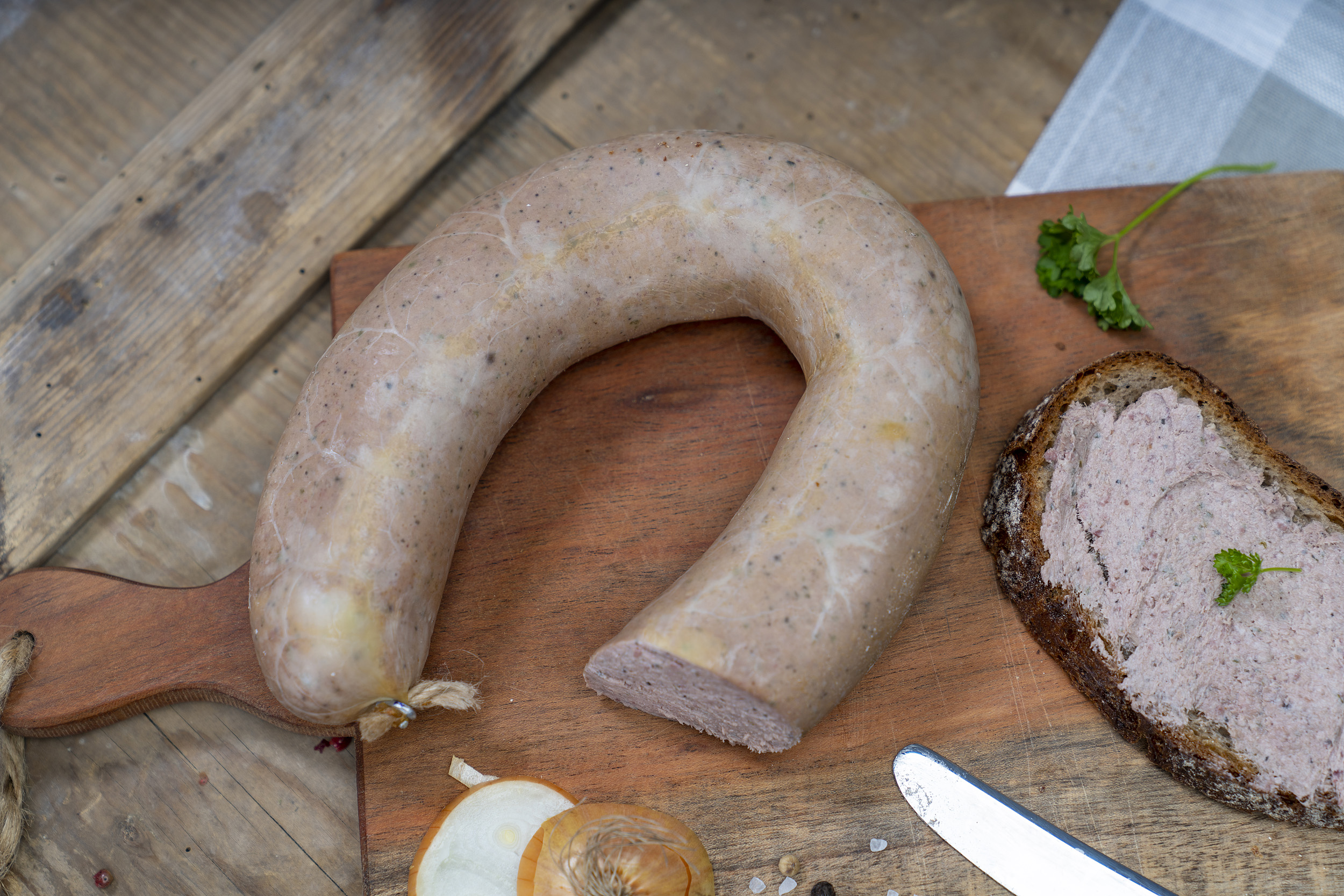 Auf einem Brett eine Leberwurst, ein geschmiertes Brot damit und Zwiebeln.