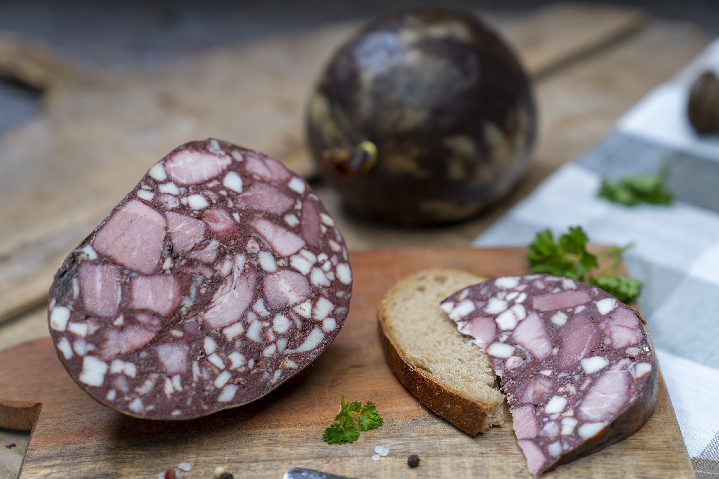 Gutsfleischwurst Auf einem Brett eine aufgeschnittene Gutsfleischwurst. Daneben eine Scheibe Brot mit der Wurst. Hinten eine weiters Blase der Wurst.