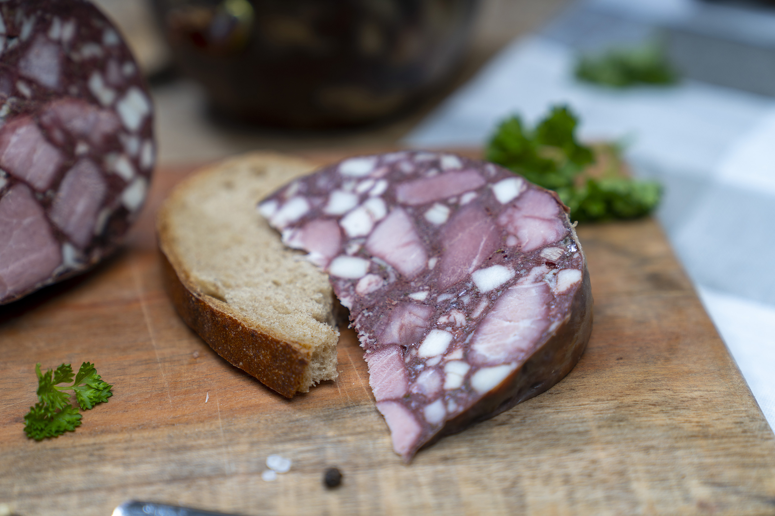 Eine Scheibe Brot mit Gutsfleischwurst. Daneben Kräuter und die Blase der Wurst.