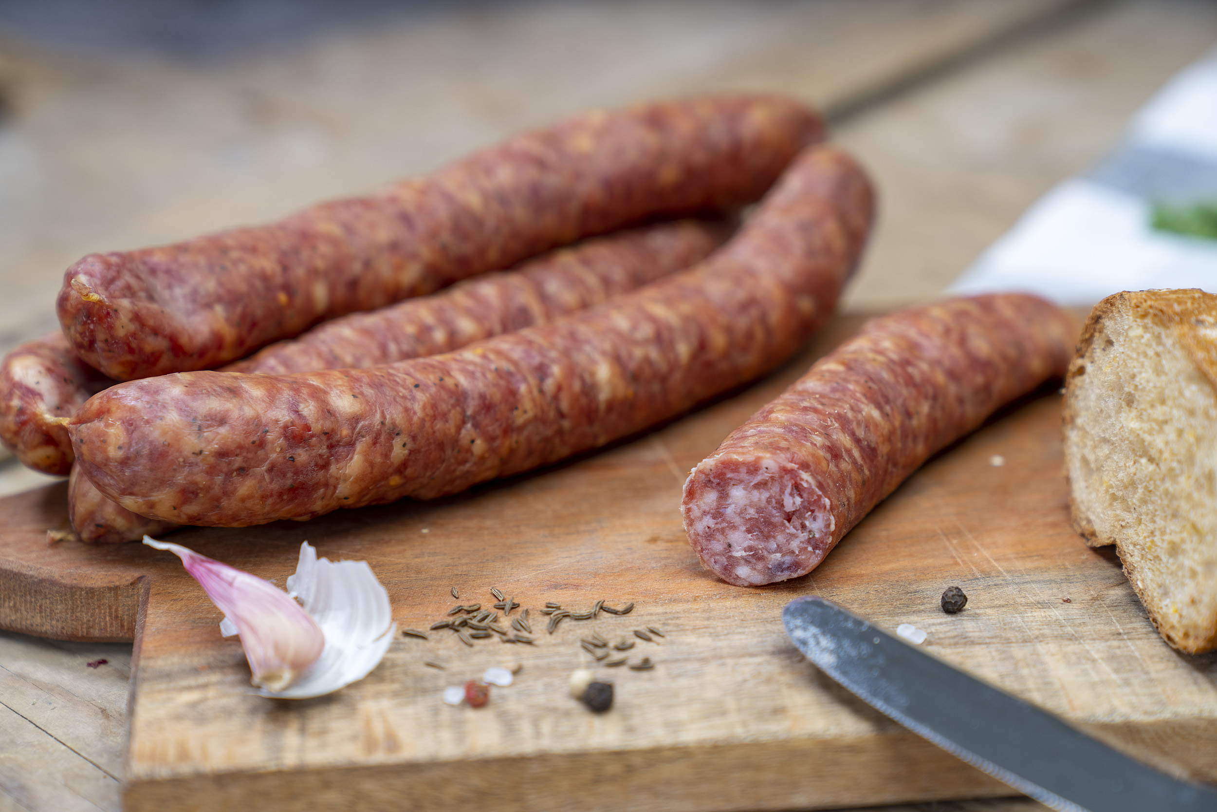 Einige Knacker auf einem Holzbrett. Daneben ein Brot und Gewürze.