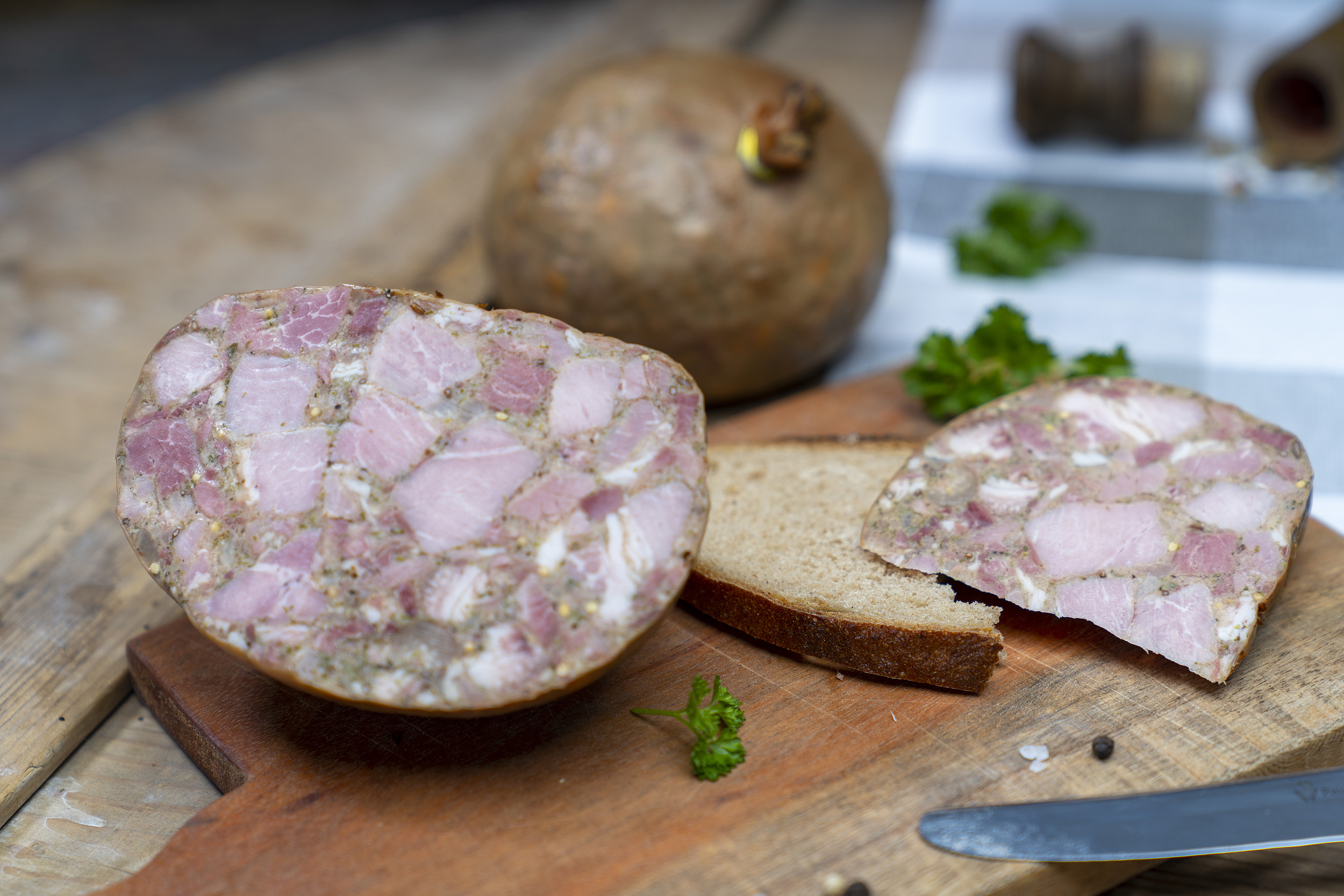 Blasensülze Eine Scheibe mit Sülze auf einem Brett. Daneben die angeschnittene Blase der Wurst und Gewürze. Hinten eine weitere Blase.